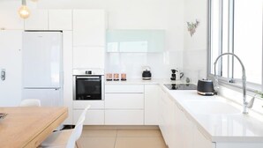 Une cuisine moderne avec des meubles blancs, un four encastré, une machine à café et une grande fenêtre.
