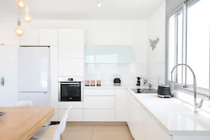 Eine moderne Küche mit weißen Schränken, einem eingebauten Backofen, einer Kaffeemaschine und einem großen Fenster.