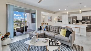 A modern living room with a sectional sofa, a coffee table, and a balcony with a view of the city.