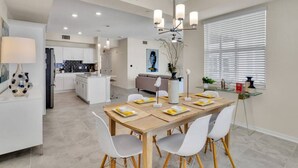 A modern kitchen with white cabinets, a central island, and a dining area with a wooden table and chairs.