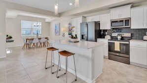 A modern kitchen with white cabinetry, stainless steel appliances, and a central island with stools.