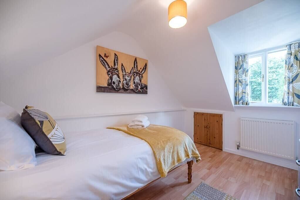 A bedroom with a bed, a painting of donkeys, a window with curtains, and a radiator.