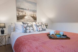 Une chambre à coucher avec un lit, des oreillers, un plateau avec de la nourriture et des boissons, un tableau au mur et une lampe sur une table de chevet.