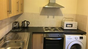 A compact kitchen with a sink, stove, microwave, and a built-in washing machine. - Impeccable 3-bed Apartment in Stockton-on-tees (Stockton-on-Tees)