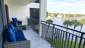 En balkon med fletmøbler og blå hynder, med udsigt over en lysthavn med både og palmer.