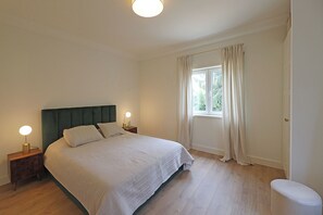 A bedroom with a bed, two bedside tables with lamps, a window with curtains, and a radiator.