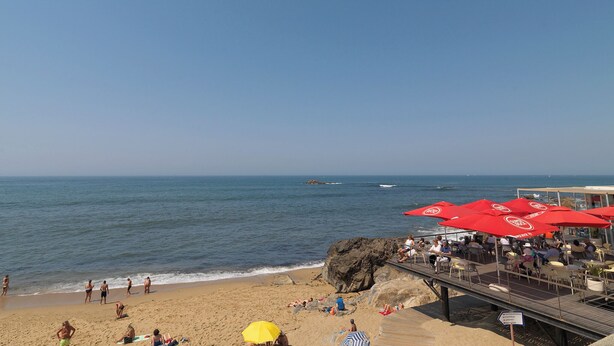 A beach with red umbrellas, a wooden walkway, and people relaxing. - FLH Serralves House with Garden (Oporto)
