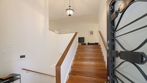 A staircase with wooden steps and a metal railing, a hanging light fixture, and a closed door with a metal gate. - FLH Serralves House with Garden (Oporto)