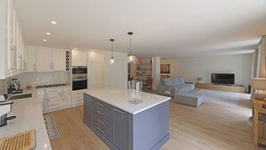 A modern kitchen with white cabinets, a central island, and a dining area with a sofa and TV. - FLH Serralves House with Garden (Oporto)