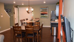 A dining area with a wooden table and chairs, a chandelier, and a kitchen area with a refrigerator and cabinets. - Comfortable, Beautiful Townhome in quaint neighborhood w/ patio deck (Henrico)