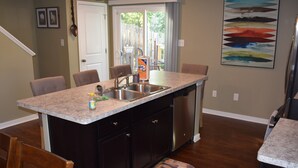 A kitchen with a granite countertop, stainless steel sink, and a dishwasher. There are four chairs around the island and a dining table in the background. - Comfortable, Beautiful Townhome in quaint neighborhood w/ patio deck (Henrico)