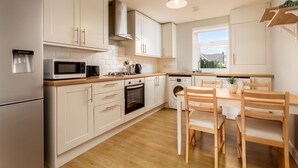 A modern kitchen with white cabinets, a microwave, a stove, a sink, and a dining area with wooden chairs and a table. - Shore View - Donnini Apartments (Prestwick)