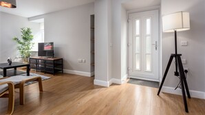 A modern living room with hardwood flooring, a dining area with a table and chairs, a standing lamp, a television, and a potted plant. - Shore View - Donnini Apartments (Prestwick)