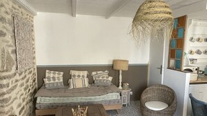 Een knus ingerichte kamer met een vloer met patroon, een houten tafel, een bank met kussens, een rieten stoel en een hanglamp.