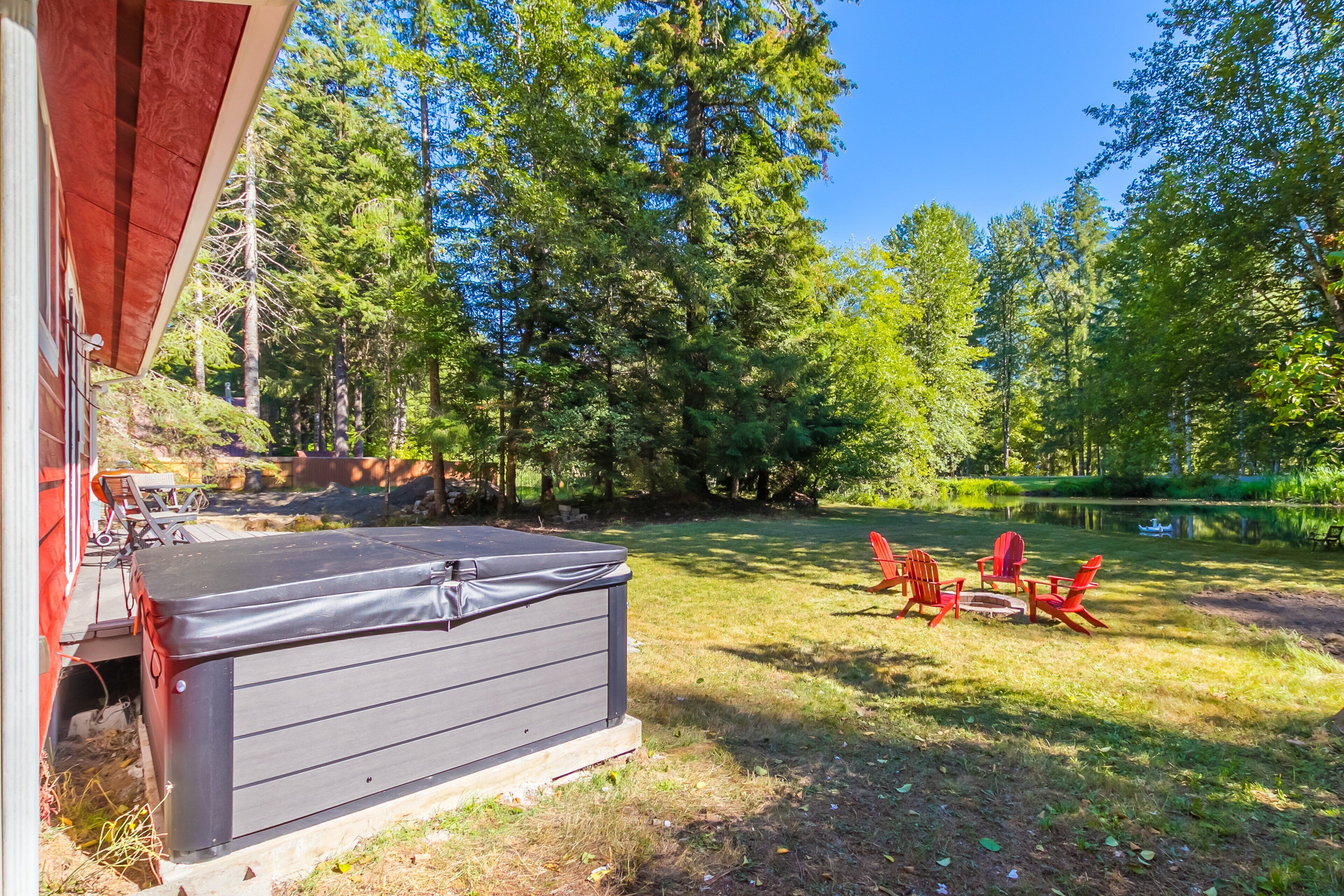 A backyard with a hot tub, outdoor furniture, and a pond.
