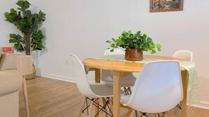 Ein Essbereich mit einem Holztisch, weißen Stühlen, einem Topfpflanzen und einem gerahmten Bild an der Wand.
