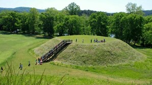 Ein großer, grasbewachsener Hügel mit einer hölzernen Brücke, die zu einem kleinen Hügel führt.