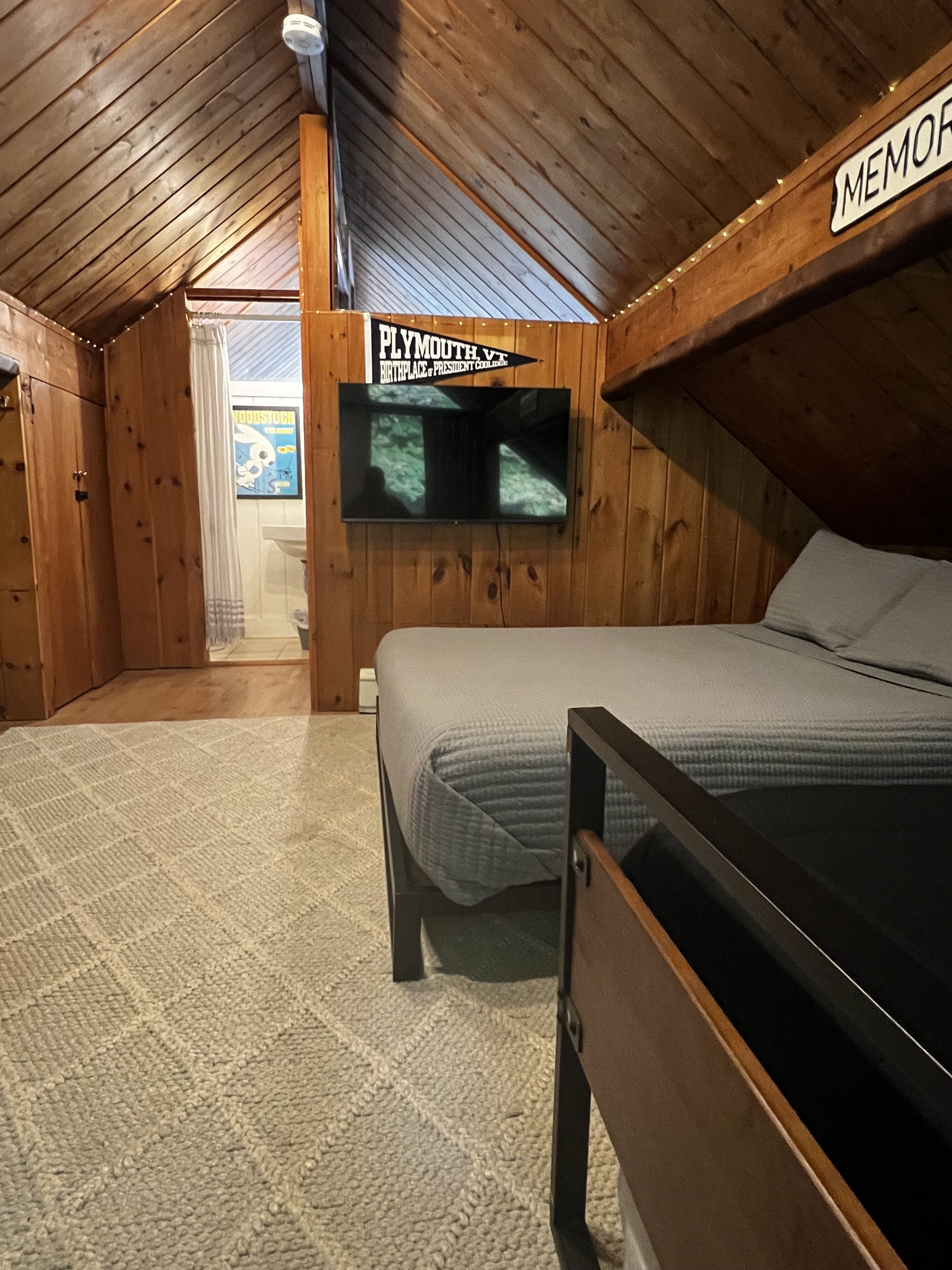 A cozy room with a bed, a TV mounted on the wall, and a wooden ceiling.