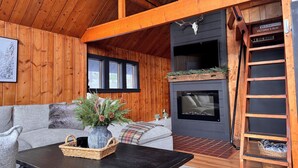 Een gezellig cabin interieur met een open haard, houten balken, een bank en een salontafel.