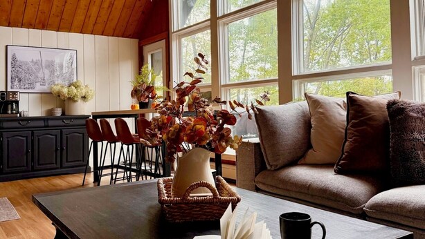 Een knus interieur met een houten plafond, grote ramen, een bank, een eettafel en een keukenhoek.