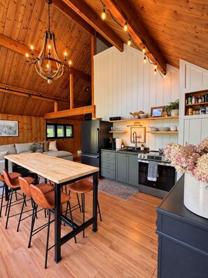 Een moderne keuken met houten kastjes, een eethoek met een houten tafel en stoelen, en een hanglamp.