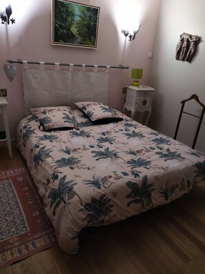 Quarto com cama, mesa de cabeceira, cadeira, quadro e luminária na parede.