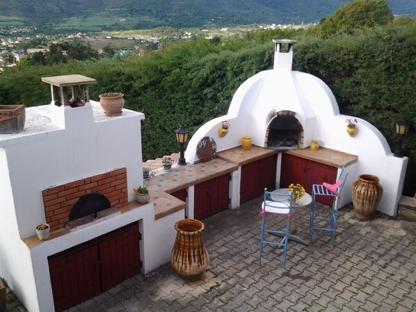 Uma cozinha externa com forno de tijolos, uma mesa e uma cadeira.