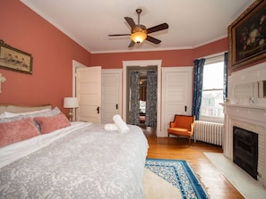 A bedroom with a bed, a chair, a fireplace, and a ceiling fan.