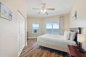 A bedroom with a bed, a ceiling fan, a window with a view, and a door.