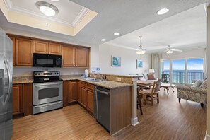 A modern kitchen with granite countertops, stainless steel appliances, wooden cabinets, and a dining area with a view.