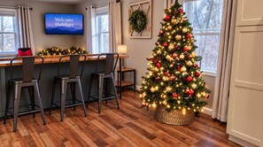 A dining area with a Christmas tree, a TV displaying 'Welcome Holidays,' and a wreath on the wall. -  10 Min Liberty University|Family Friendly w/King&Patio/Grill|Playset (FOREST)