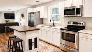 A modern kitchen with stainless steel appliances, white cabinetry, a wooden island, and a bar seating area. - Modern Family Haven 10 Min to Liberty/ King Bed•Patio•Grill•Firepit•Playset (FOREST)