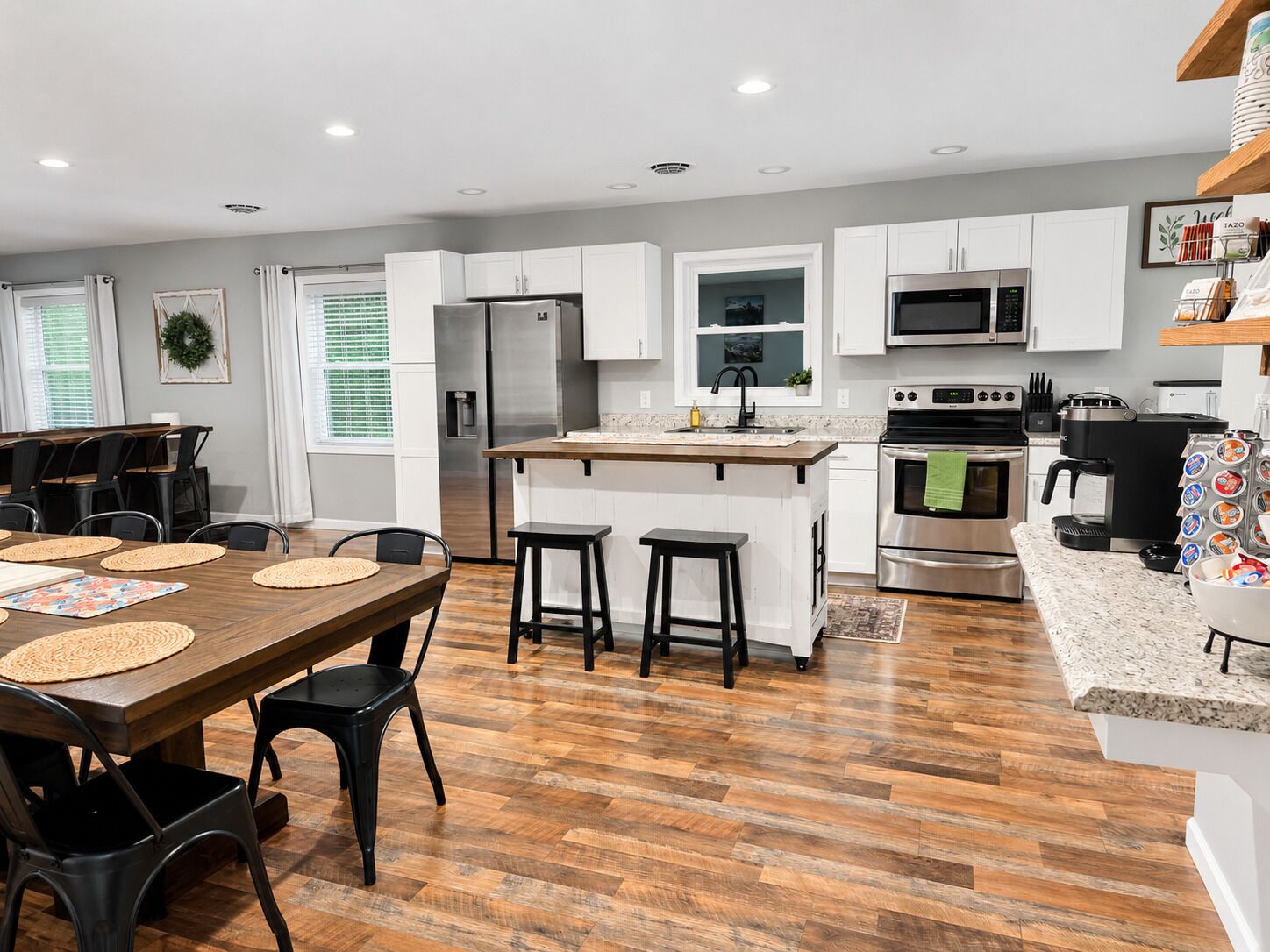 A modern kitchen with white cabinets, stainless steel appliances, and a wooden dining table with black chairs.