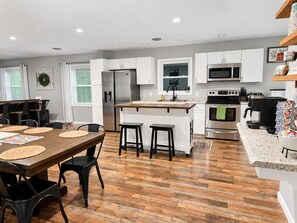 A modern kitchen with white cabinets, stainless steel appliances, and a wooden dining table with black chairs. -  10 Min Liberty University|Family Friendly w/King&Patio/Grill|Playset (FOREST)