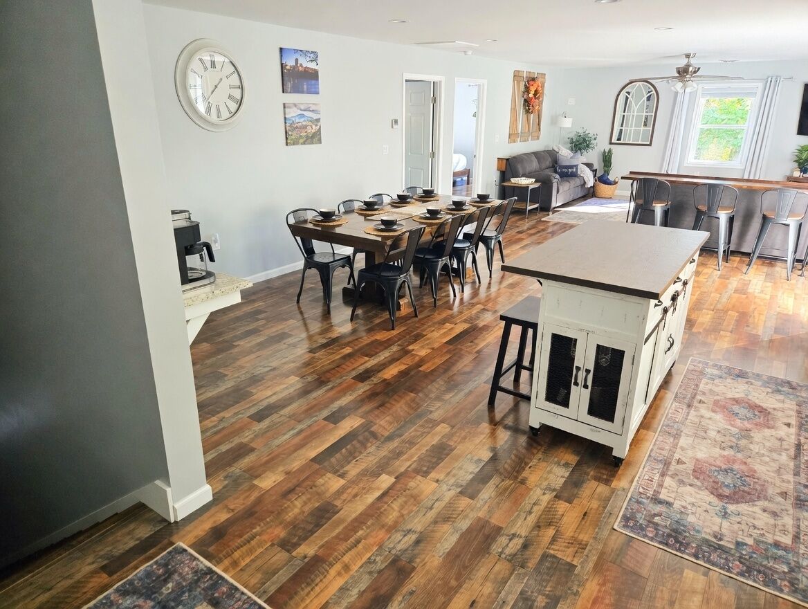 A spacious kitchen with a dining area, wooden flooring, and a clock on the wall.