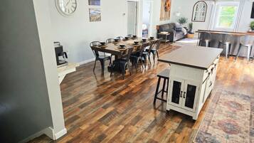 A spacious kitchen with a dining area, wooden flooring, and a clock on the wall.