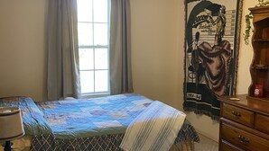 Um quarto com cama, cômoda, janela com cortinas, pôster na parede e luminária no teto.