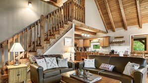 A spacious living room with a staircase, leather sofas, wooden coffee table, and a kitchen in the background. - Beautiful Views of the Smoky Mountains! Hot Tub-Game Room-3 King Beds-Sleeps 11 (Sevierville)