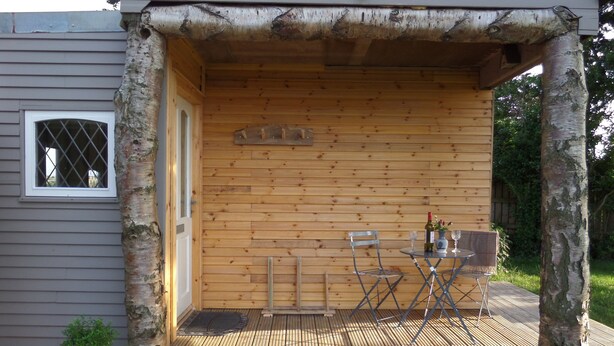 A wooden deck with a table and chairs, a small potted plant, and a window with bars. - Charming 1-bed Garden Lodge in Boyndie, Banff (Banff)