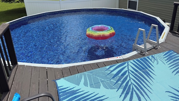 Ein oberirdischer Swimmingpool mit einem bunten Schwimmreifen, einer Holzterrasse und einer Sicherheitsleiter.