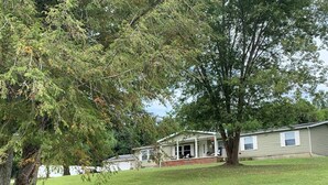 Ein Bungalow mit Veranda und einem großen Baum davor.