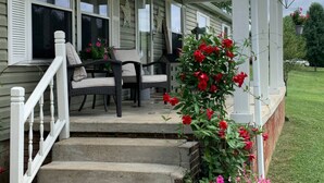 Eine überdachte Veranda mit einer Treppe zu einer Sitzgruppe, bestehend aus zwei Stühlen und einem Tisch.