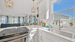 A modern kitchen with white cabinetry, a stainless steel sink, and a large window overlooking a residential area. - Just Peachy - 4 BR/3BA Private Pool (Santa Rosa Beach)