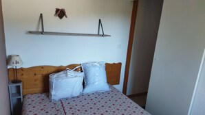 Ein Schlafzimmer mit einem Holz-Kopfteil, einem Bett mit gemustertem Bettbezug, zwei Kissen, einem Nachttisch mit Lampe und einem Wandregal über dem Bett.