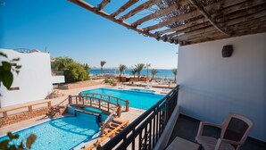Un área de piscina en la azotea con un puente de madera, sillas de descanso y vistas al mar.
