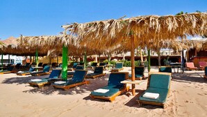 Un resort frente a la playa con tumbonas bajo sombrillas de paja, una playa de arena y un cielo azul despejado.