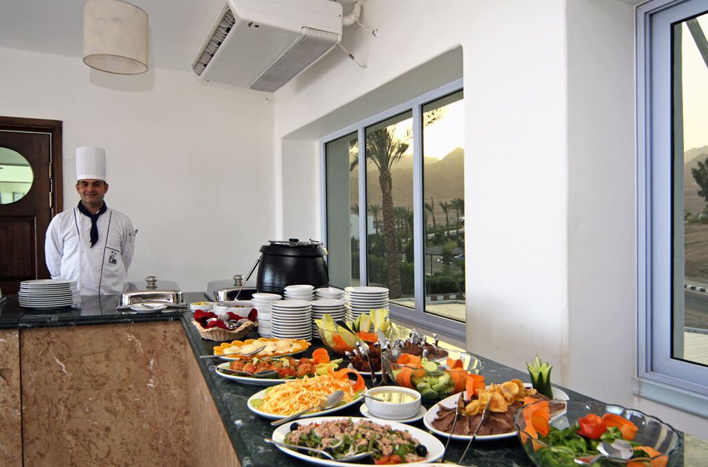 A buffet setup with various dishes and a chef standing by the counter.
