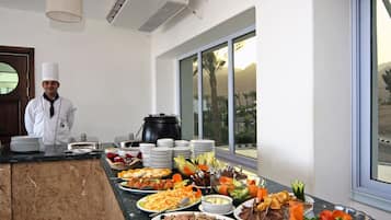 A buffet setup with various dishes and a chef standing by the counter.