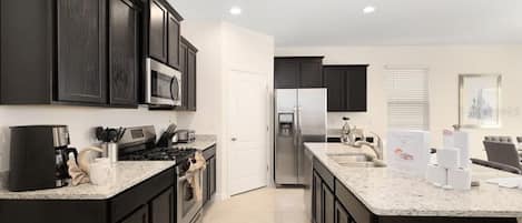 A modern kitchen with dark cabinetry, a central island, stainless steel appliances, and a large window.
