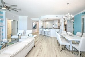Uma sala de estar moderna com um sofá branco, uma mesa de centro de vidro e um espaço de refeições com cadeiras e mesa brancas.